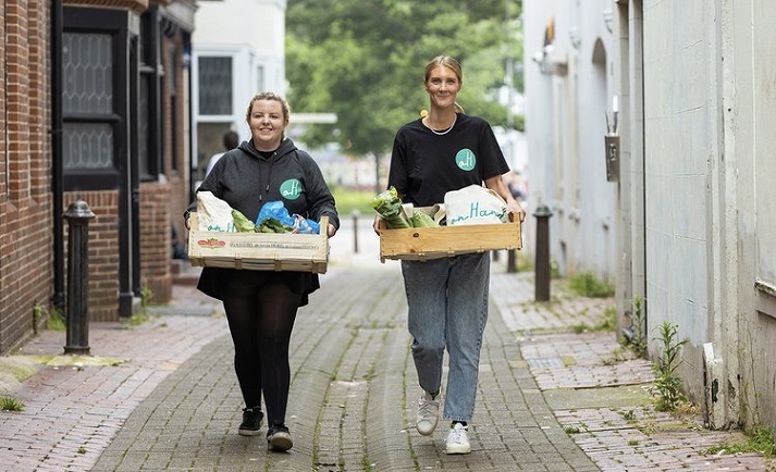 Two females volunteering for onHand walking through a street carrying hampers full of fresh food