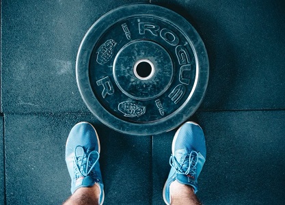 Cropped shot of male feet wearing blue gym trainers standing next to a round weight